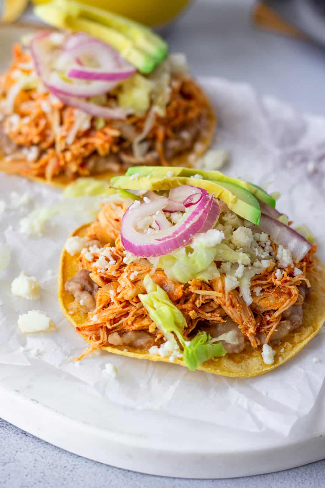 Two tostadas on a board with parchment paper.