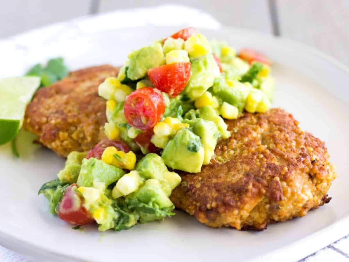 Horizontal view of 2 salmon cakes on a white plate with avocado corn salsa on top.