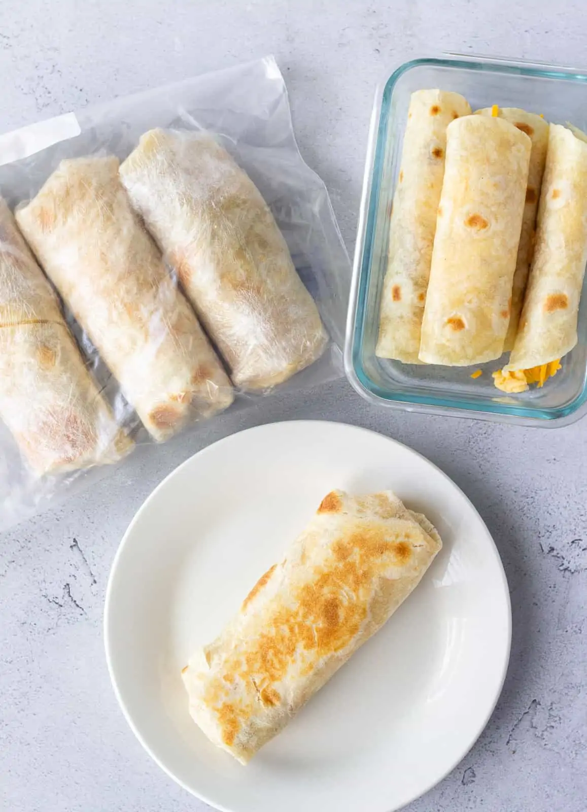 1 burrito on a round white plate, small burritos in a glass dish, and 3 burritos wrapped in plastic wrap in a bag.