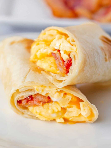 Feature image of bacon egg and cheese burrito sliced in half stacked on a plate.