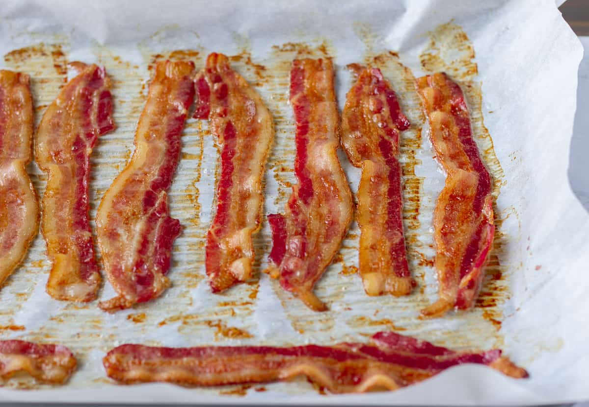 Cooked strips of bacon on parchment lined baking sheet.