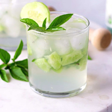 Clear glass with pieces of cucumber and garnished with basil leaves.