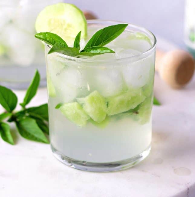Clear glass with pieces of cucumber and garnished with basil leaves.