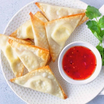 Overhead view of Cream Cheese Wontons on a round plate with a side of sweet chili sauce.