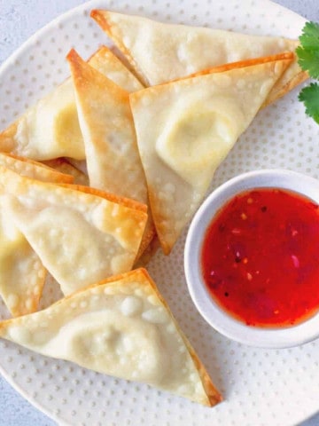 Overhead view of Cream Cheese Wontons on a round plate with a side of sweet chili sauce.