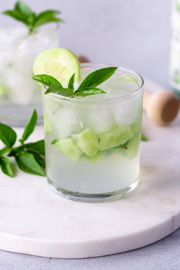 Up close view of basil and cucumber gin cocktail on a marble board.