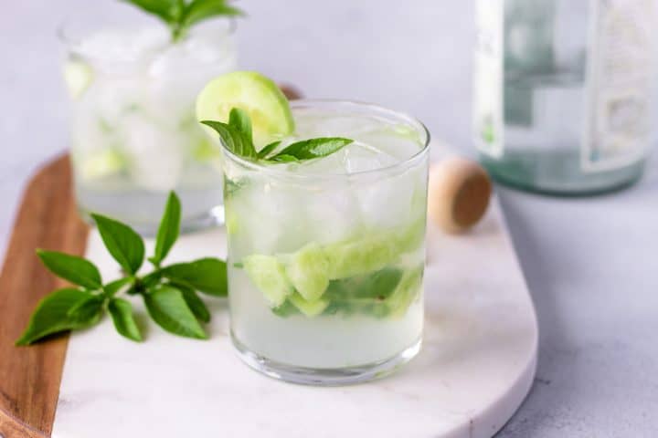 Horizontal view of 2 cocktails on a marble board with a bottle in the background.