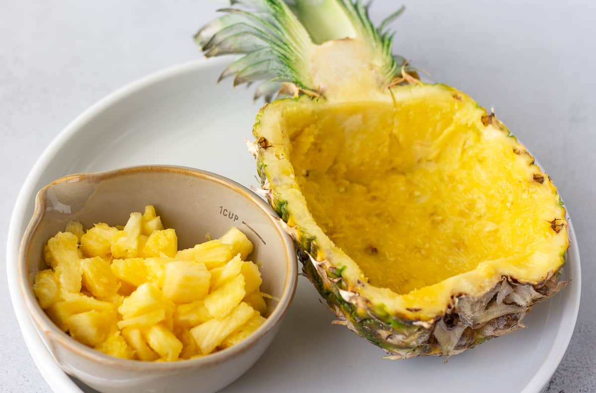 Pineapple shell hollowed out with chunks of pineapple in a small bowl.