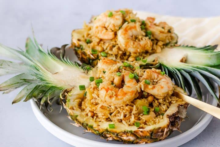 Horizontal view of fried rice in pineapple shells on a white plate with a gold spoon.