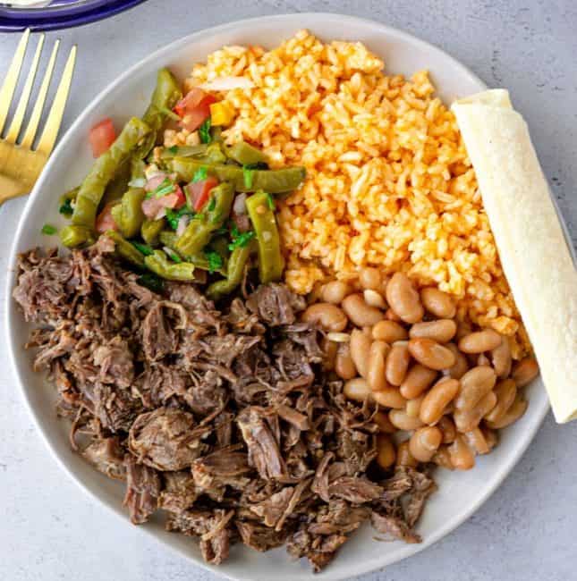 Barbacoa on a round plate with beans, rice, and cactus salad.