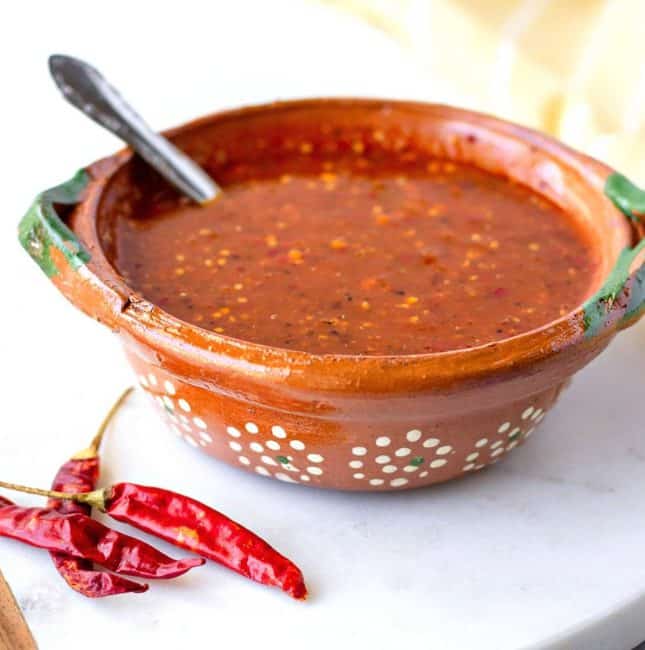 Up close view of salsa in a clay bowl with chili's on the side.