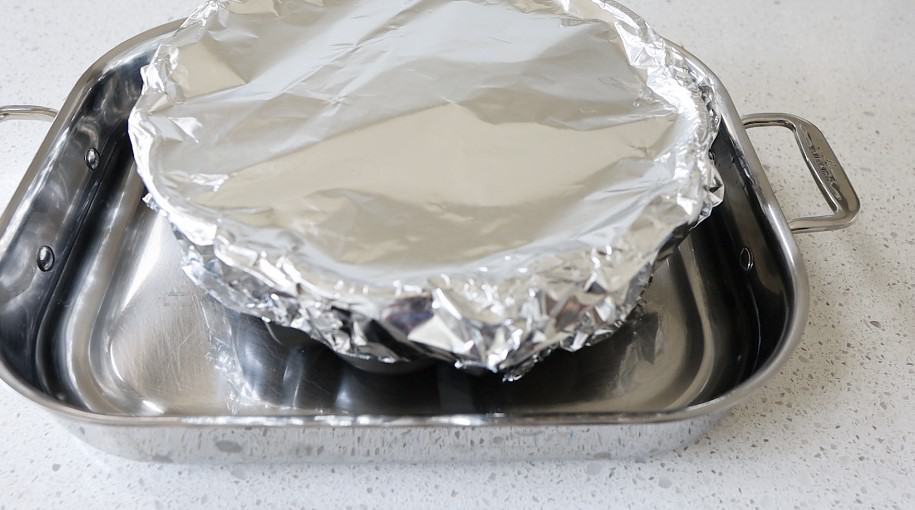 Roasting pan filled with water and bundt pan inside wrapped in foil.