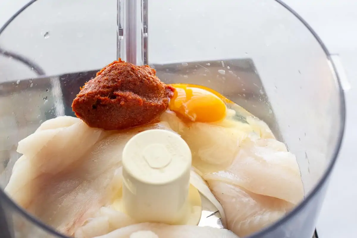 Tilapia, red curry paste, and an egg inside a food processor.