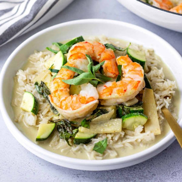 Green Curry on a plate with rice and topped with 2 pieces of shrimp.