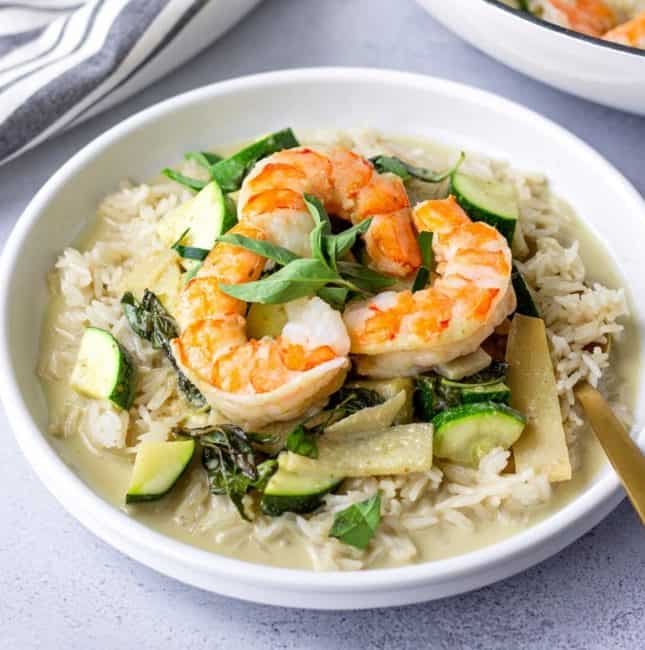 Green Curry on a plate with rice and topped with 2 pieces of shrimp.