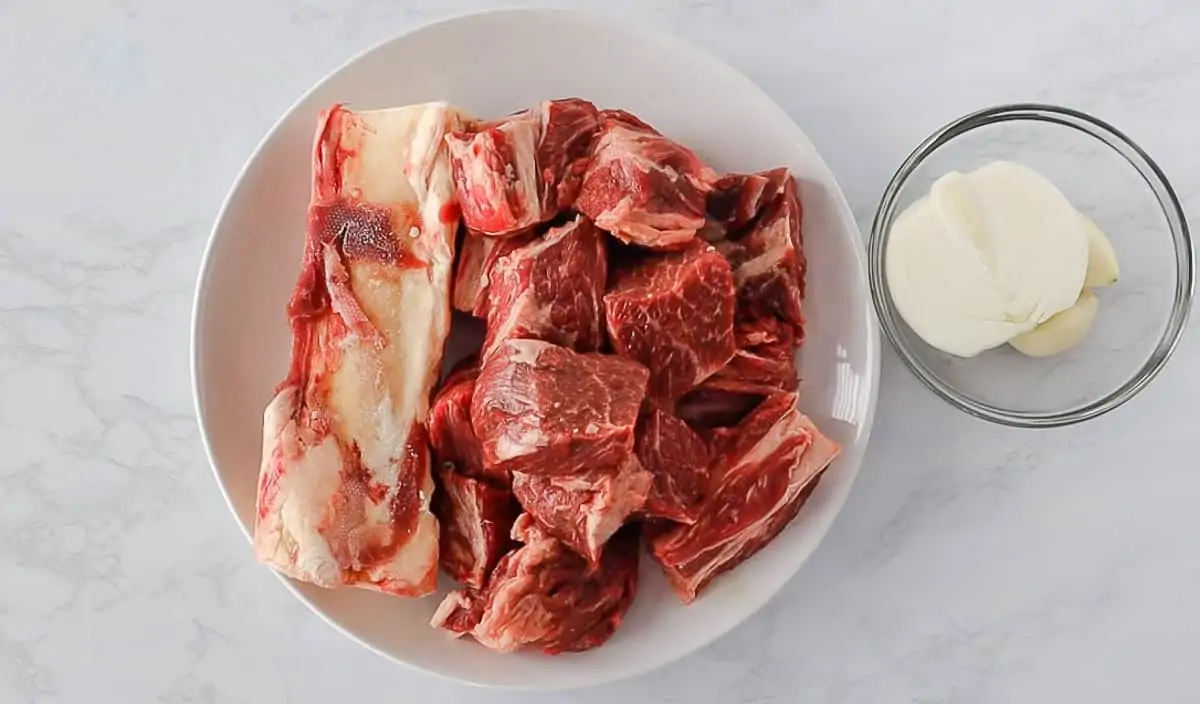 Raw beef and bones on a white round plate.
