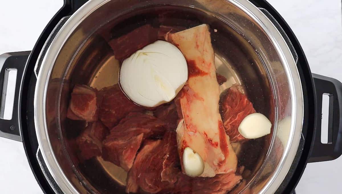 Beef, beef bones, onion, and garlic in the instant pot with water.
