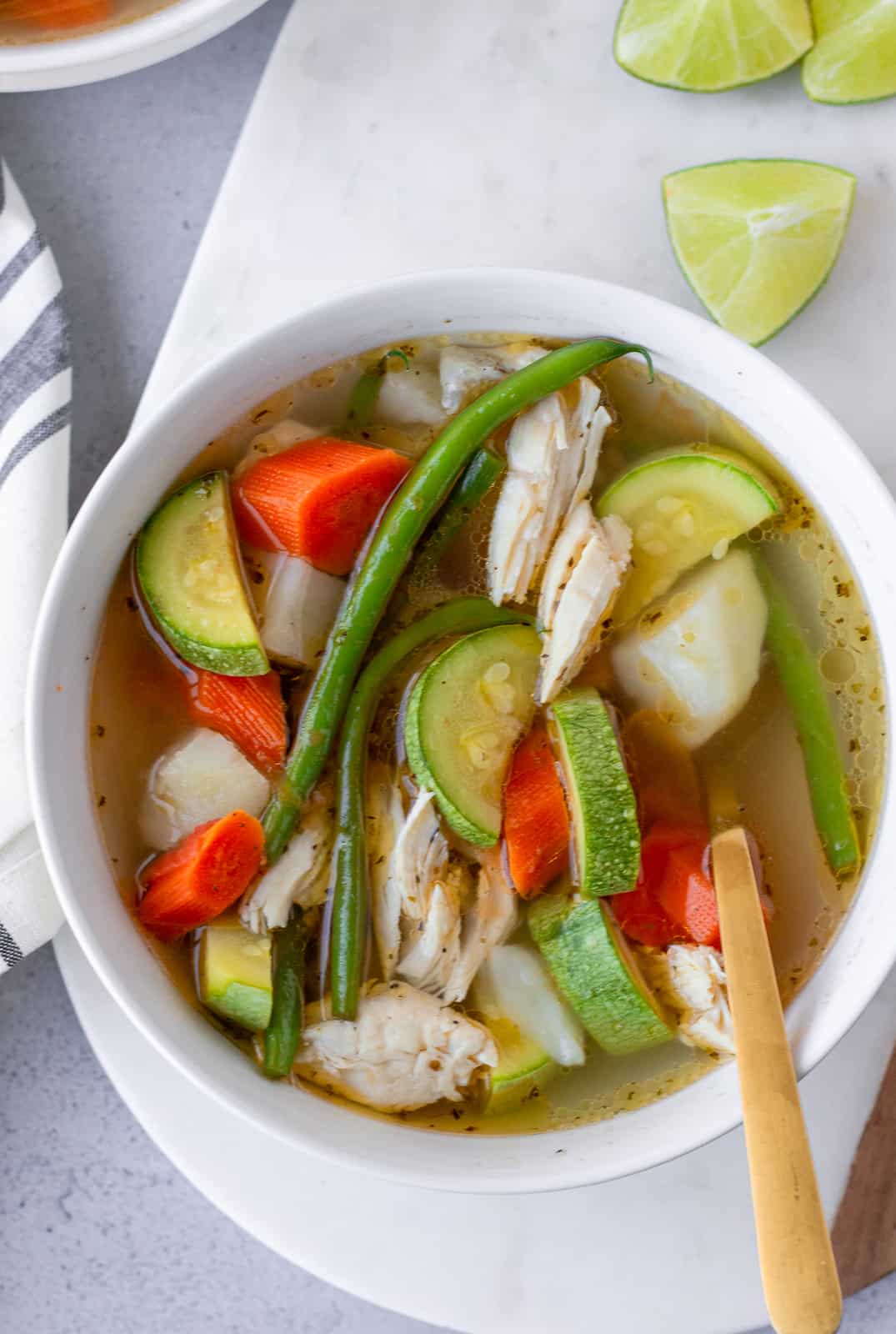 Overhead view of caldo de pollo in a white bowl with lime wedges on the side.