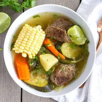 Overhead view of caldo de res in a white bowl with chunks of vegetables and beef.