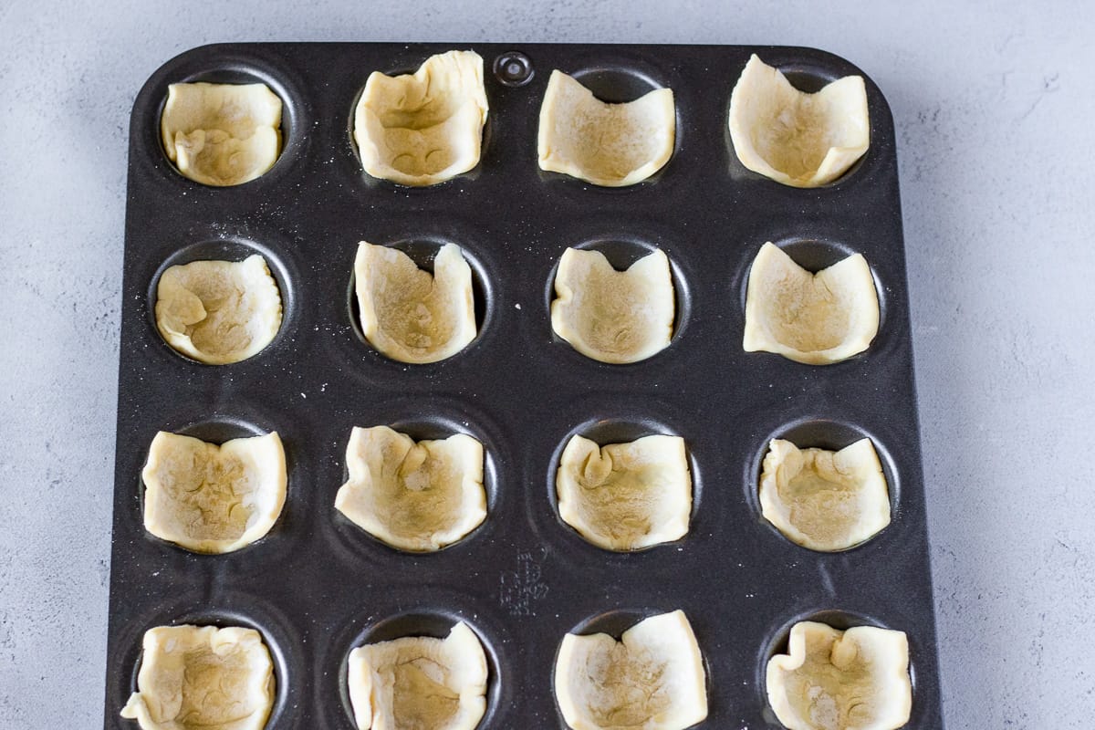 Mini muffin tin filled with a square of puff pastry.