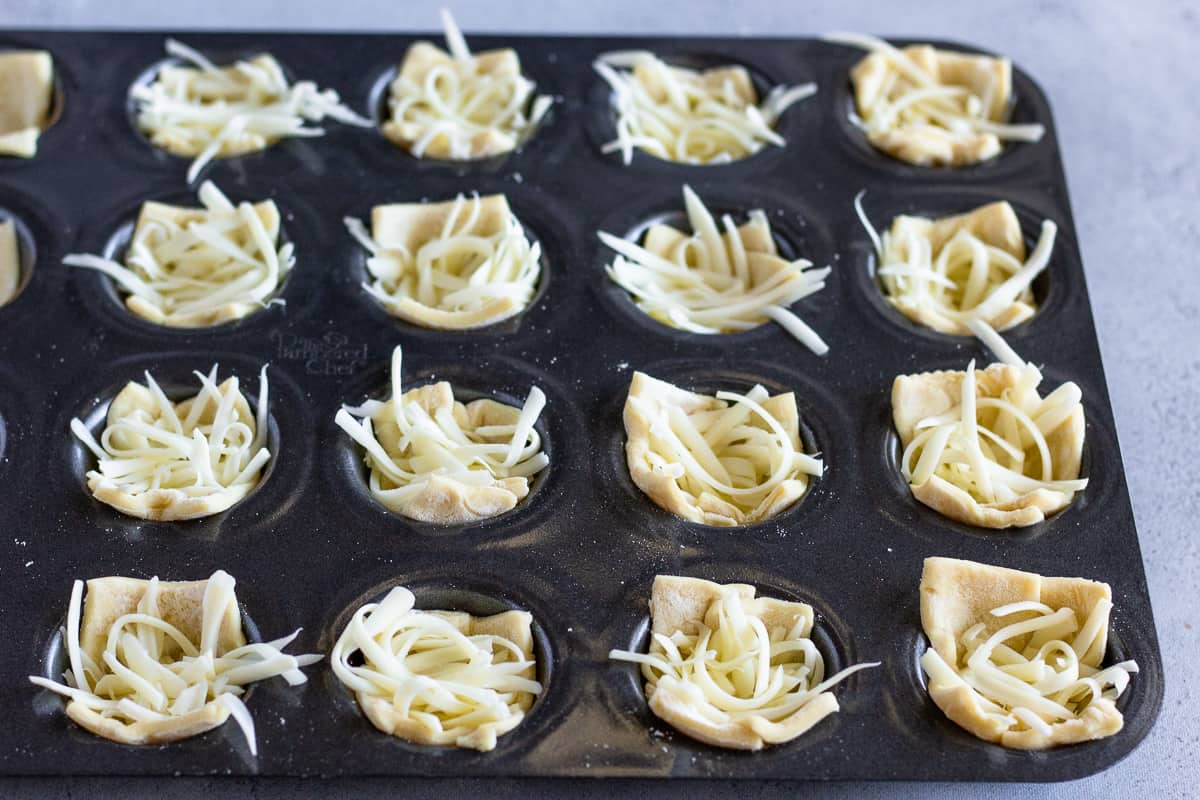 Mini muffin tin filled with puff pastry and shredded cheese.