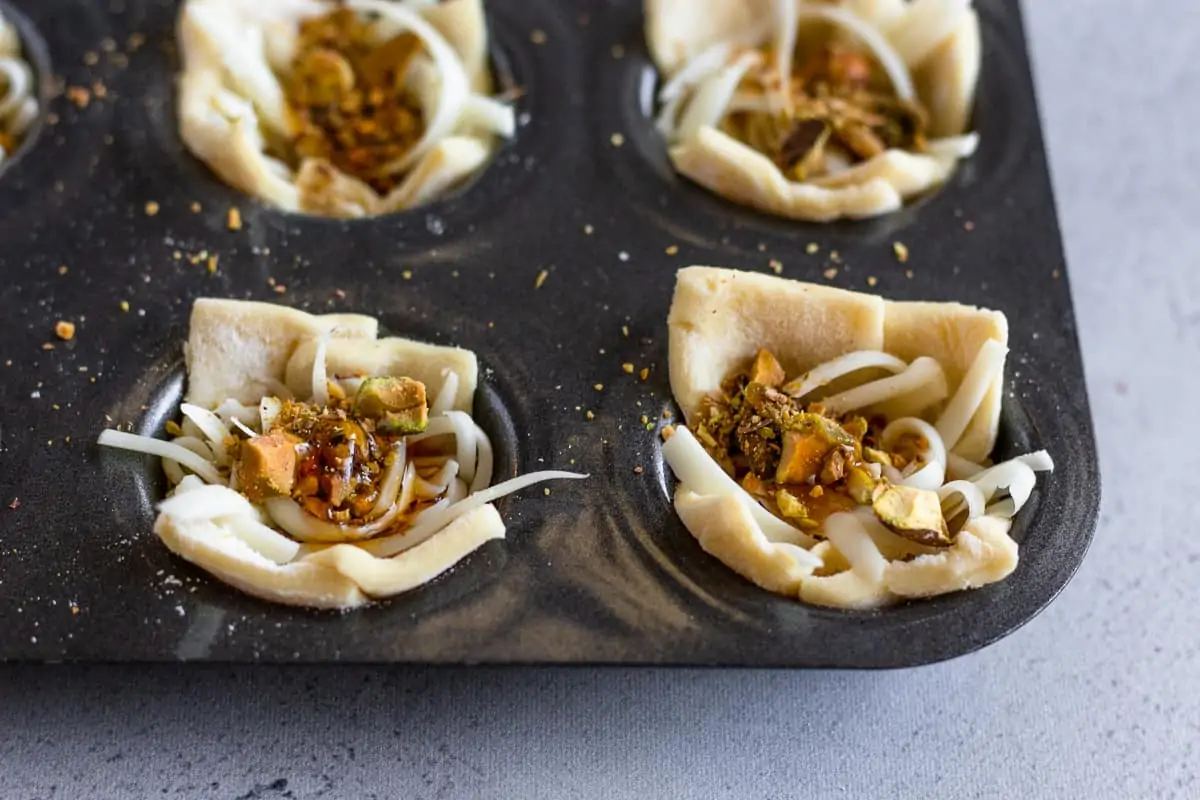 Unbaked puff pastry bites in a muffin tin.