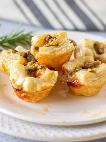 Baked puff pastry bites on a plate with honey drizzle and sprig of rosemary.