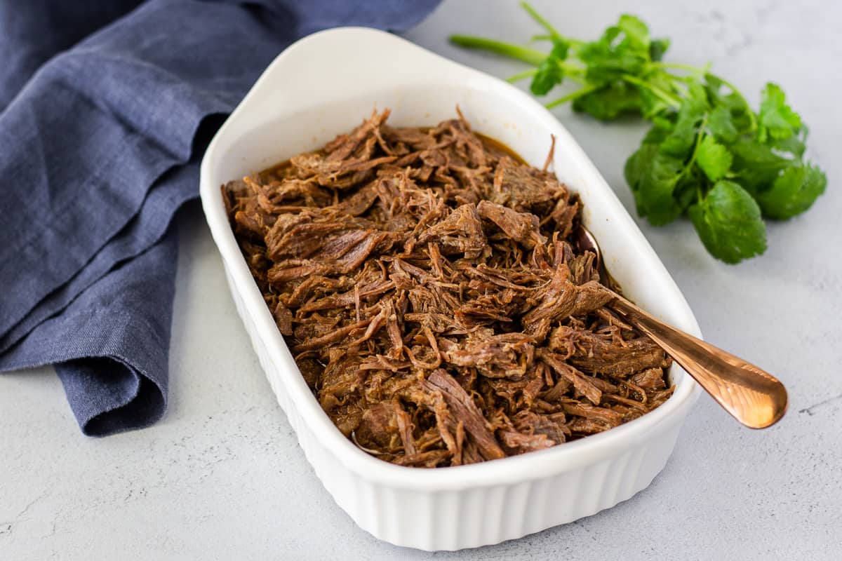 Shredded beef in a white dish with a blue napkin and cilantro on the side.