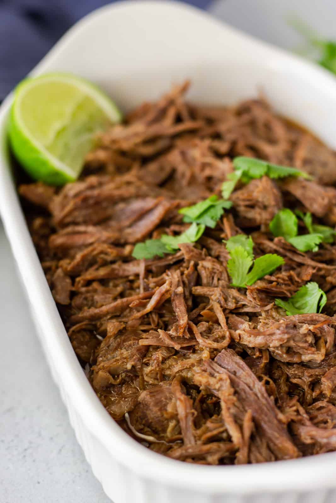 Up close view of shredded beef in a white dish topped with cilantro and a lime wedge.