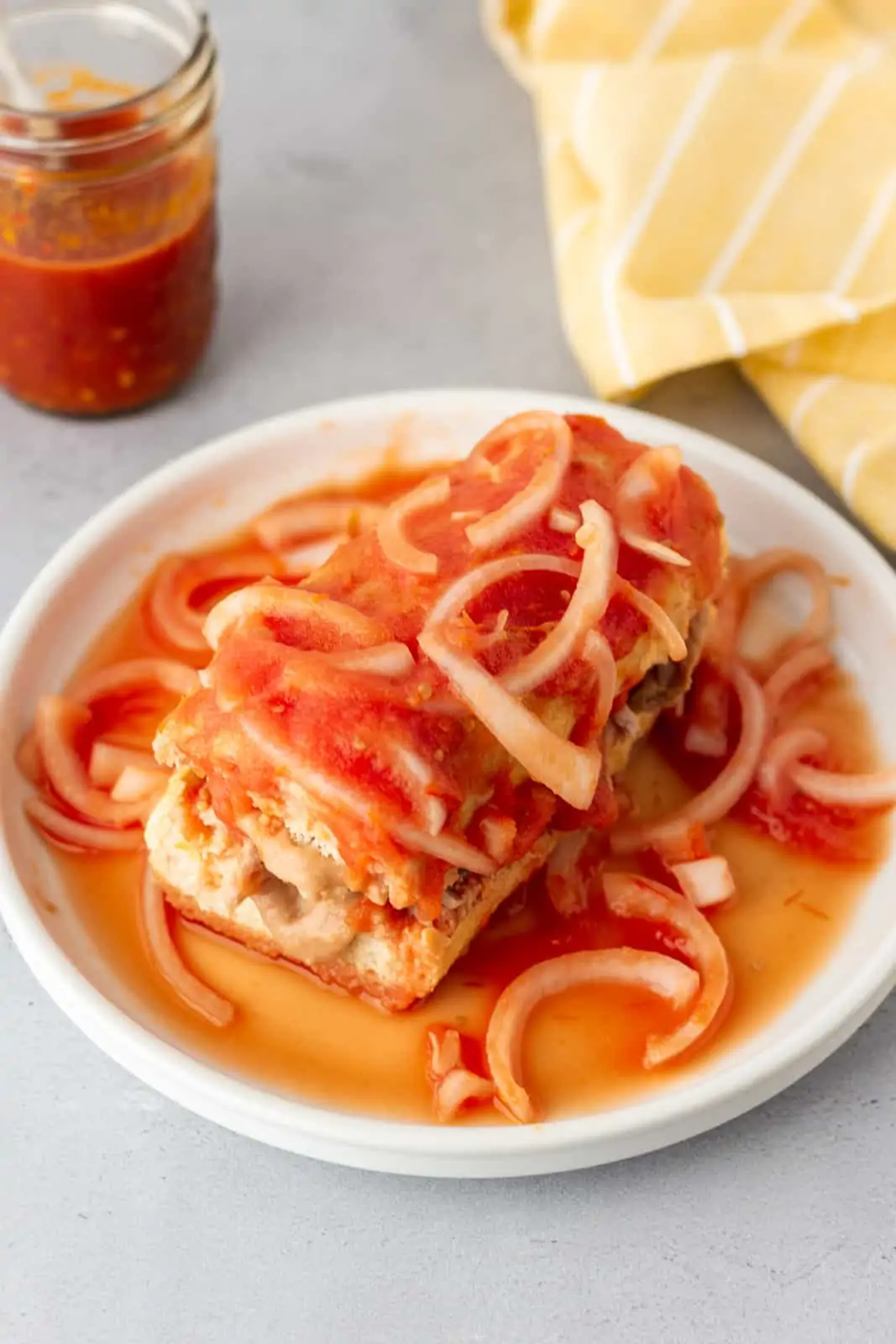 Completed Torta Ahogada on a white plate with a jar of salsa on the side.