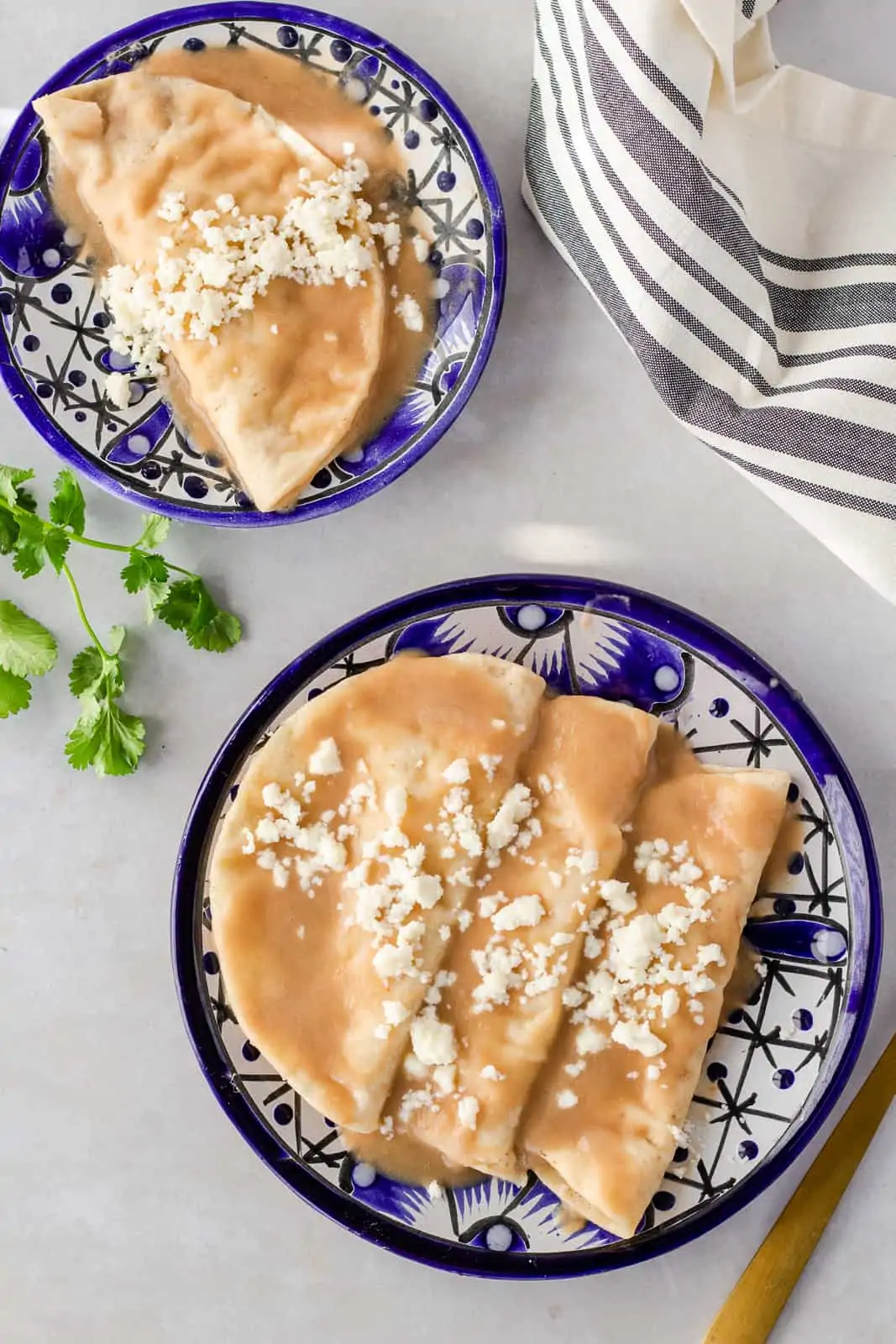 Two blue plates with bean enchiladas topped with queso fresco.