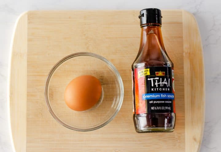 Wood cutting board with an egg and bottle of fish sauce.