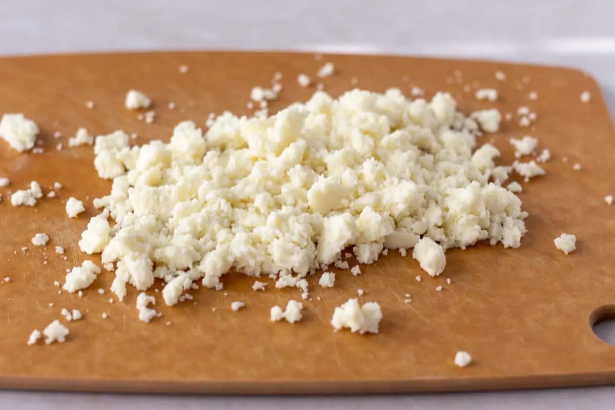 Crumbled queso fresco on a brown cutting board.