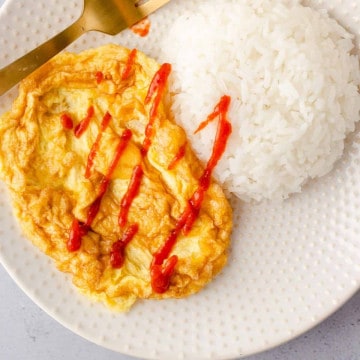 Feature image of kai jeow with rice and siracha sauce.