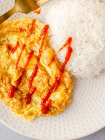 Feature image of kai jeow with rice and siracha sauce.