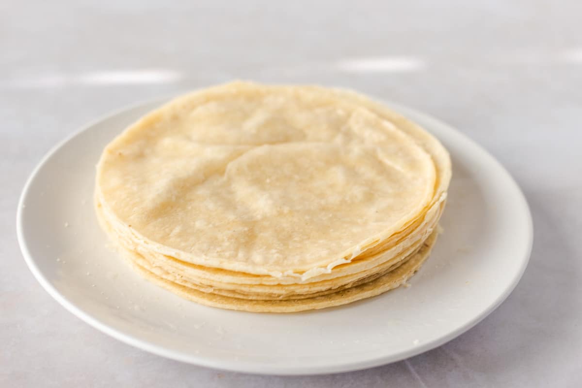 Corn tortillas stacked on a round white plate.