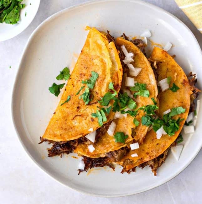 Overheard view of garnished QuesaBirria tacos on a round plate.