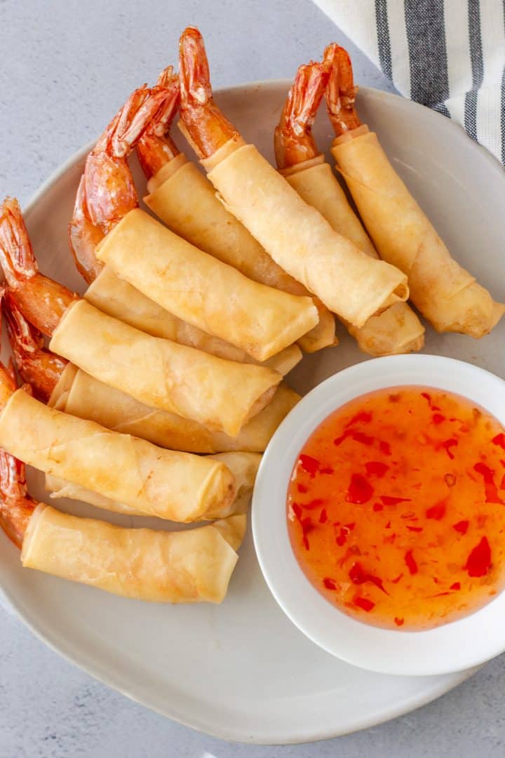 Overhead view of fried shrimp rolls on a plate with sweet chili dipping sauce.