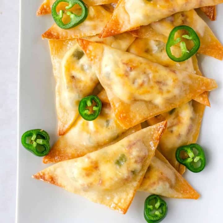 Up close view of jalapeno popper wontons on a plate with sliced jalapenos.