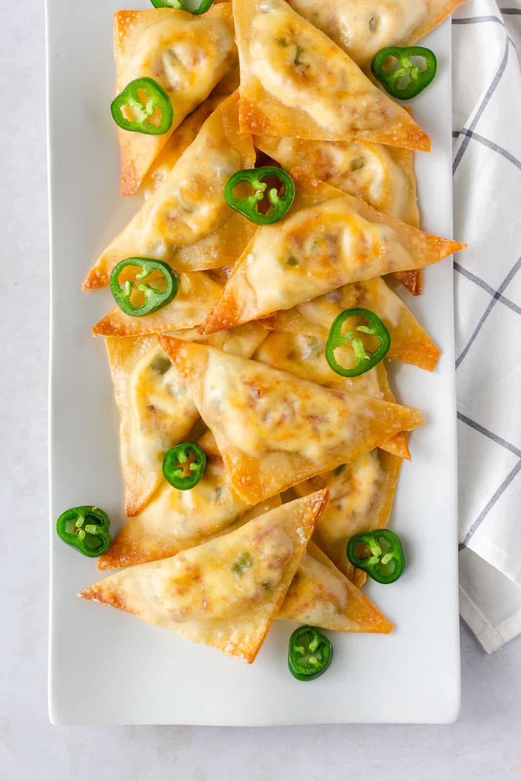 Overhead view of wontons on a white plate and garnished with jalapeno slices.