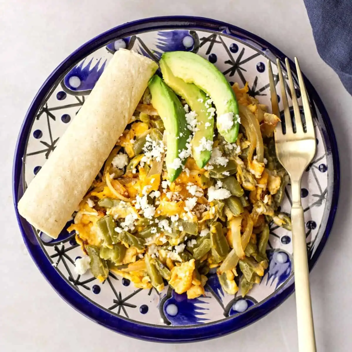 Egg and cactus on a blue plate with a tortilla on the side.