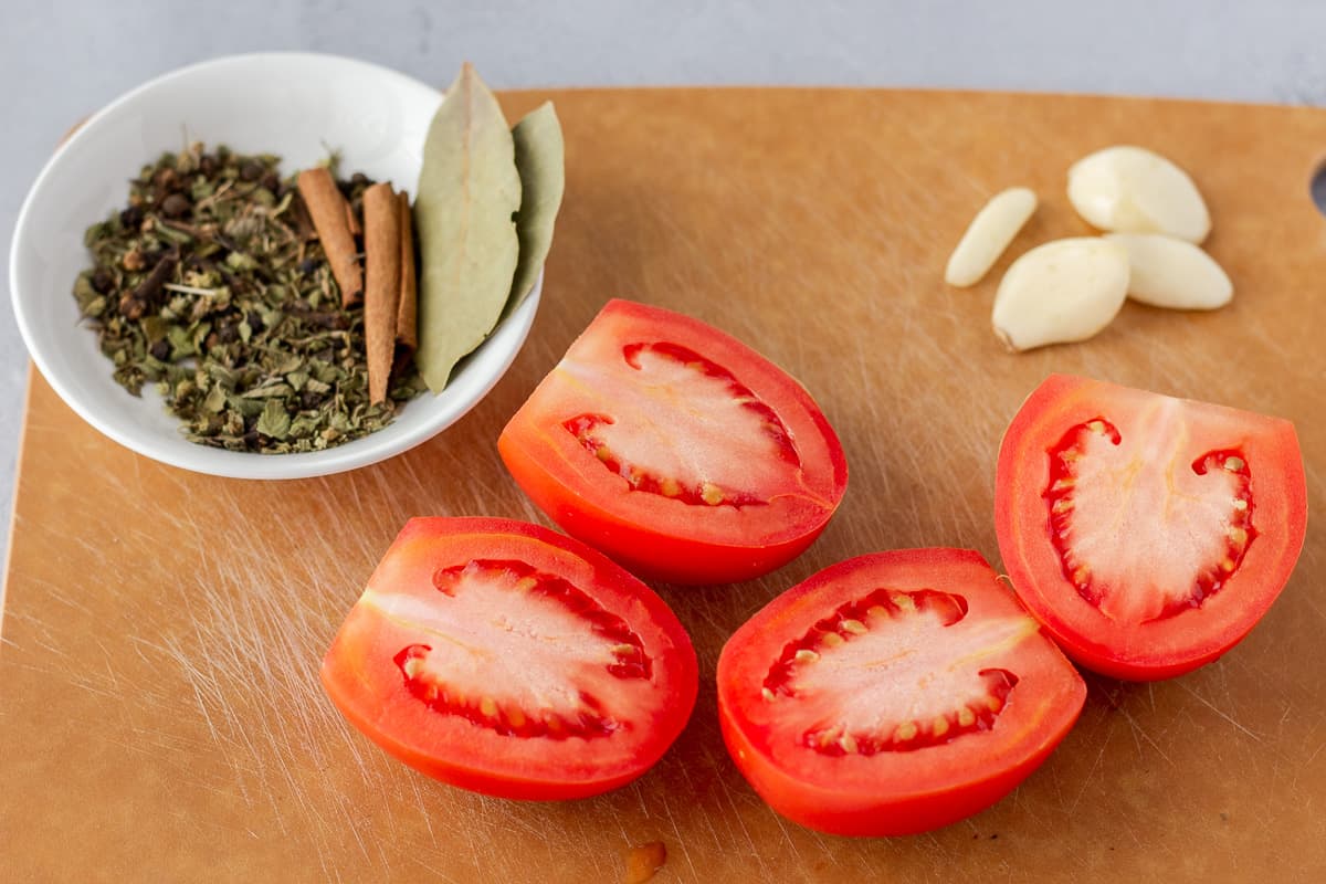 Sliced roma tomatoes, spices in a bowl, and garlic cloves.