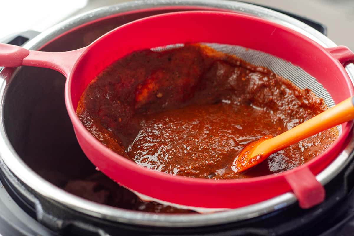 Red sauce in a strainer with a spatula.
