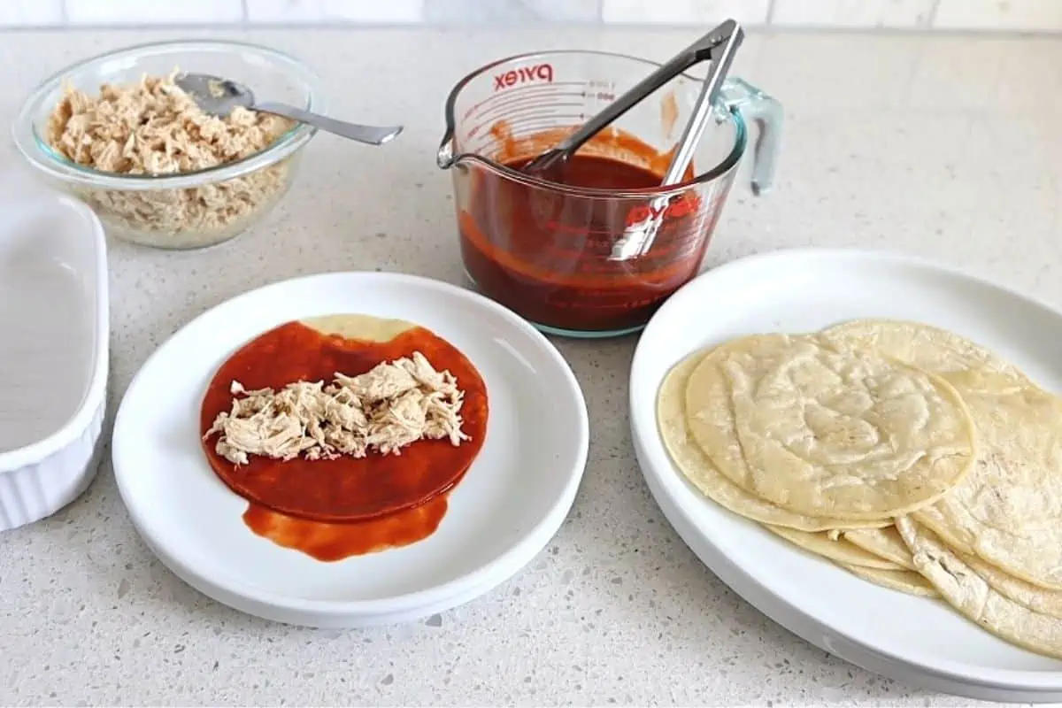 Sauce covered tortilla on a plate with shredded chicken in the middle.