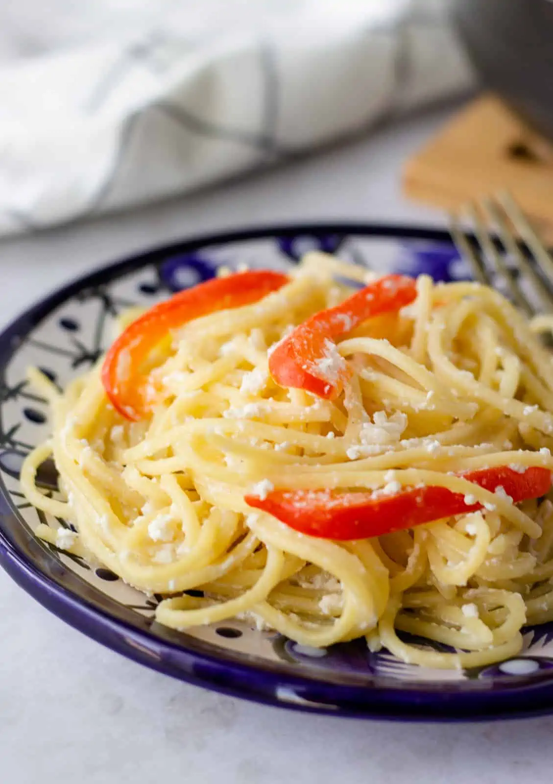 Completed Espagueti Blanco on a blue plate with red bell peppers.