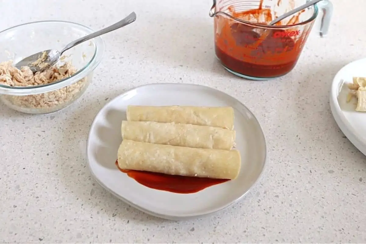 3 rolled tortillas on a plate with some red sauce on the bottom.