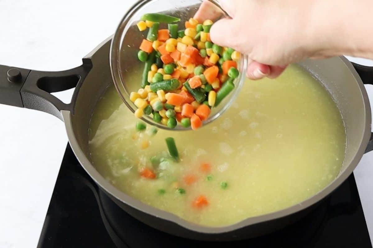 Adding mixed vegetables to pan of rice.