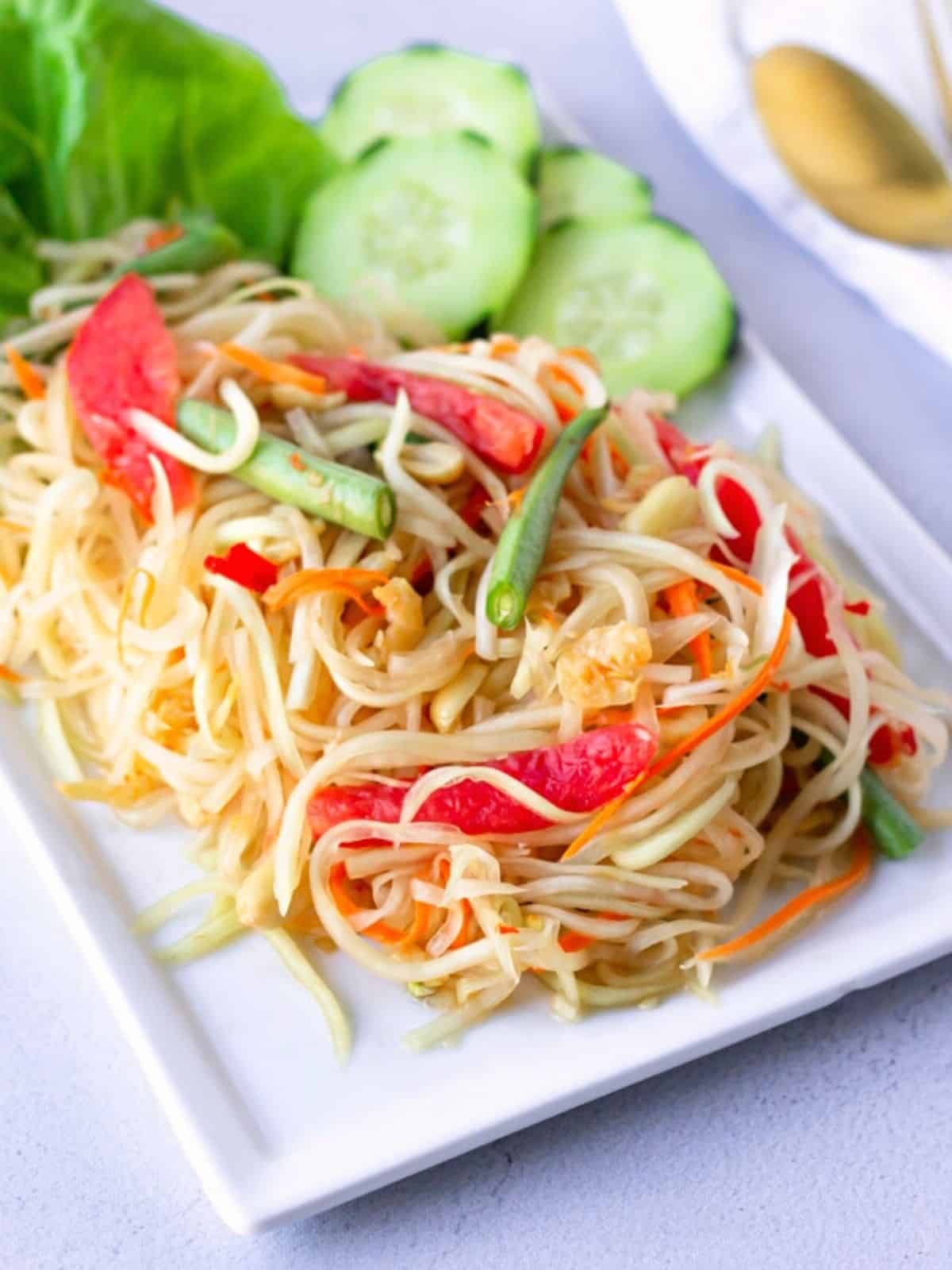 Papaya Salad on a white plate with lettuce and cucumbers.