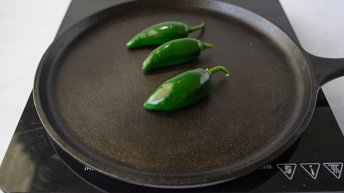 Three jalapenos on a cast iron skillet.