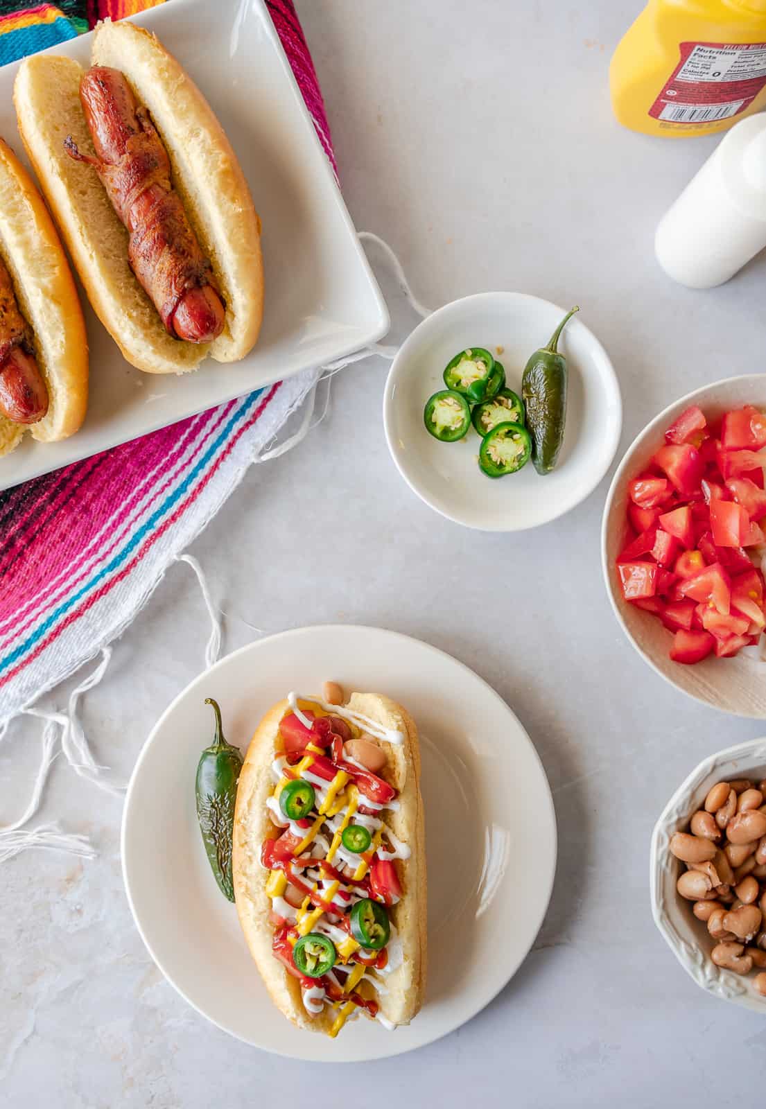 Overhead view of plain Sonoran hot dogs on a plate and one with toppings.